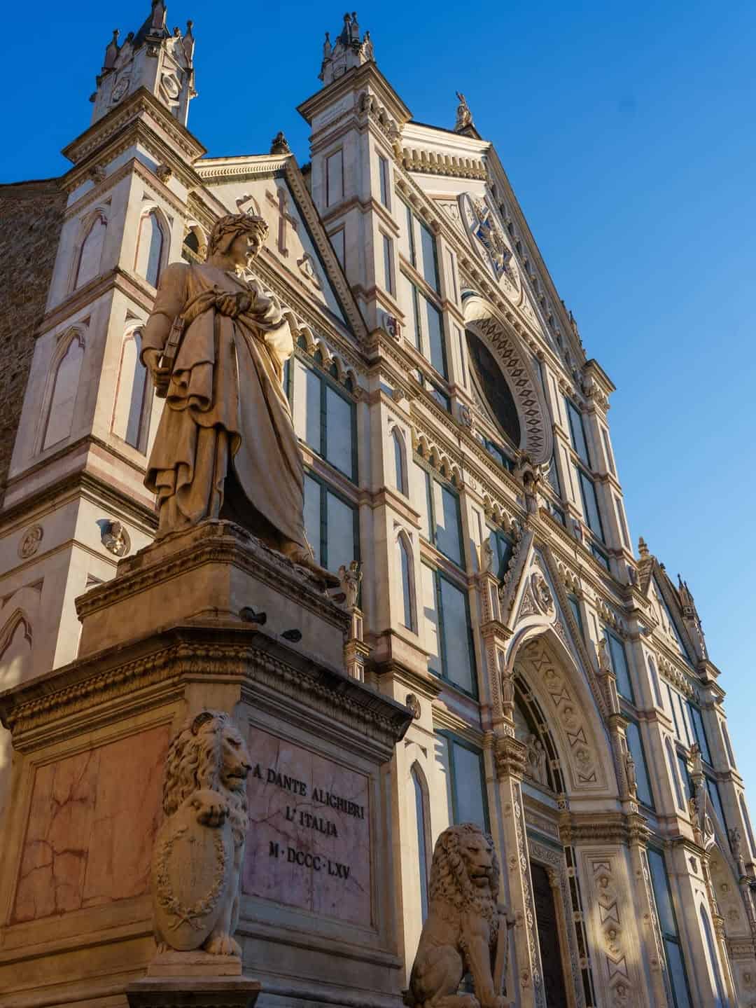 The statue of Dante Alighieri stands proudly before the Basilica di Santa Croce in Florence, a highlight on one of the best day trips from Rome for families, especially under a clear blue sky.