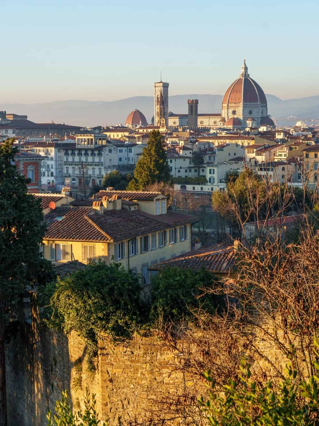 View of Florence skyline at sunset with the Florence Cathedral dome rising above historic buildings and trees&mdash;a stunning stop on one of the best day trips from Rome for families.
