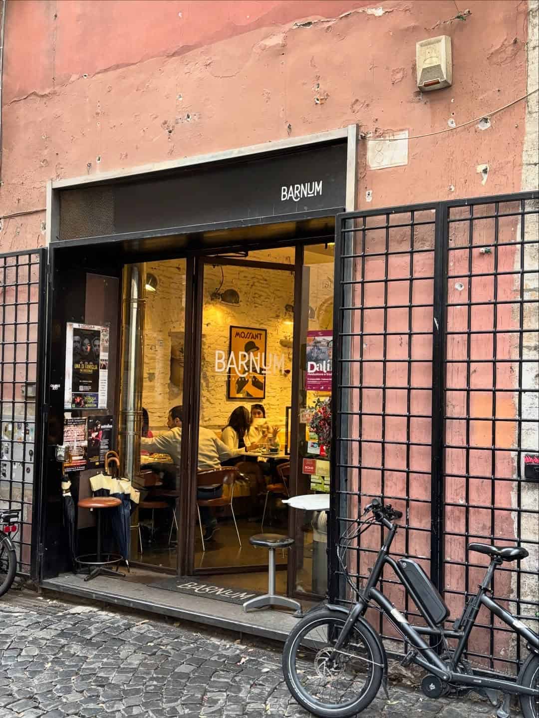 Small café called Barnum with people inside, bikes parked outside, and posters on the exterior wall—one of the cozy gluten free restaurants in Rome.