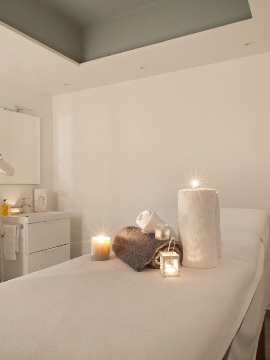 A spa treatment room with a massage table, rolled towels, candles, and soft ambient lighting&mdash;perfect for relaxing after a day at one of the best beach resorts in Italy for families.