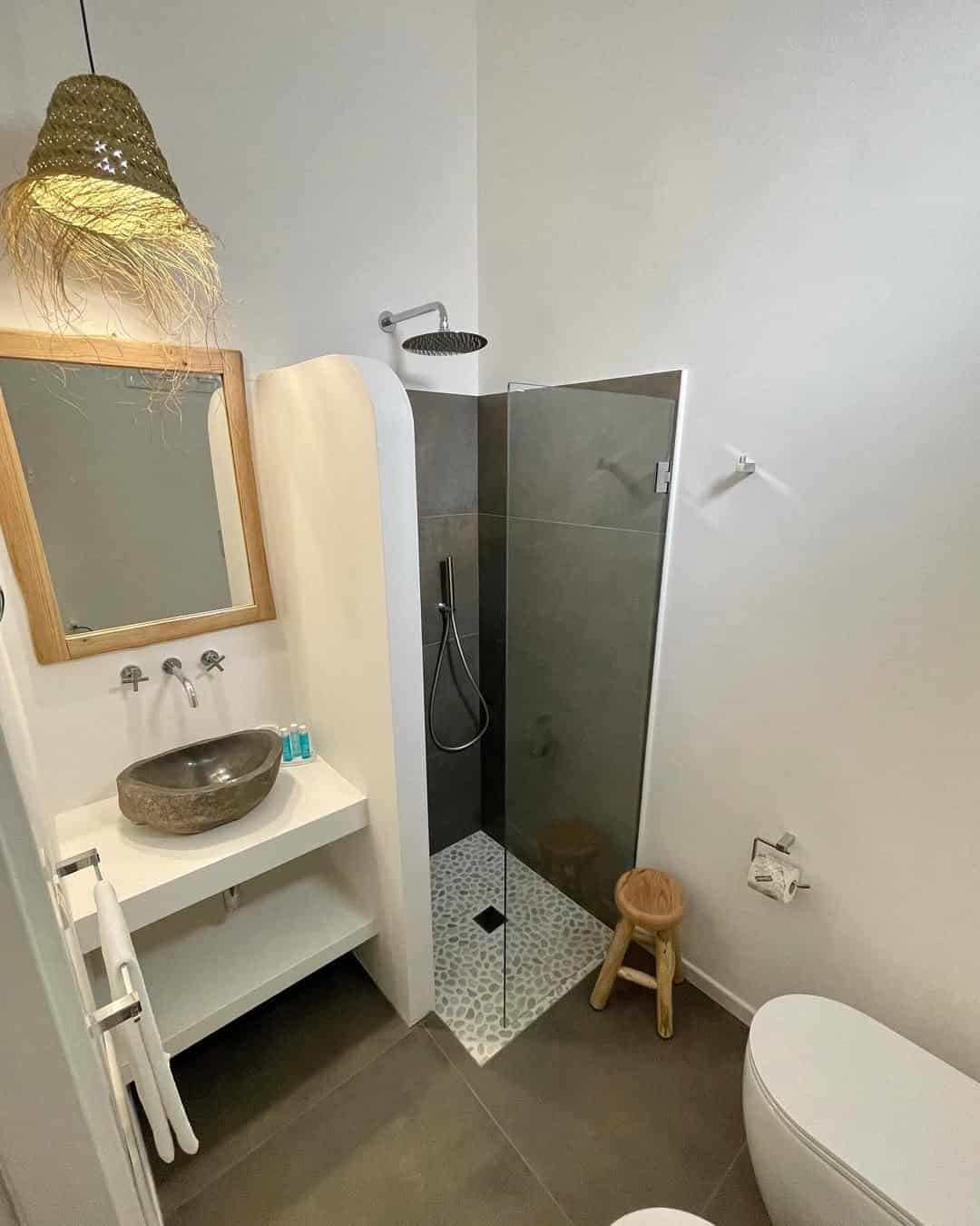 Modern bathroom with a vessel sink, walk-in shower, wooden stool, and hanging woven light fixture&mdash;reminiscent of the elegant style found in the best beach resorts in Italy for families.