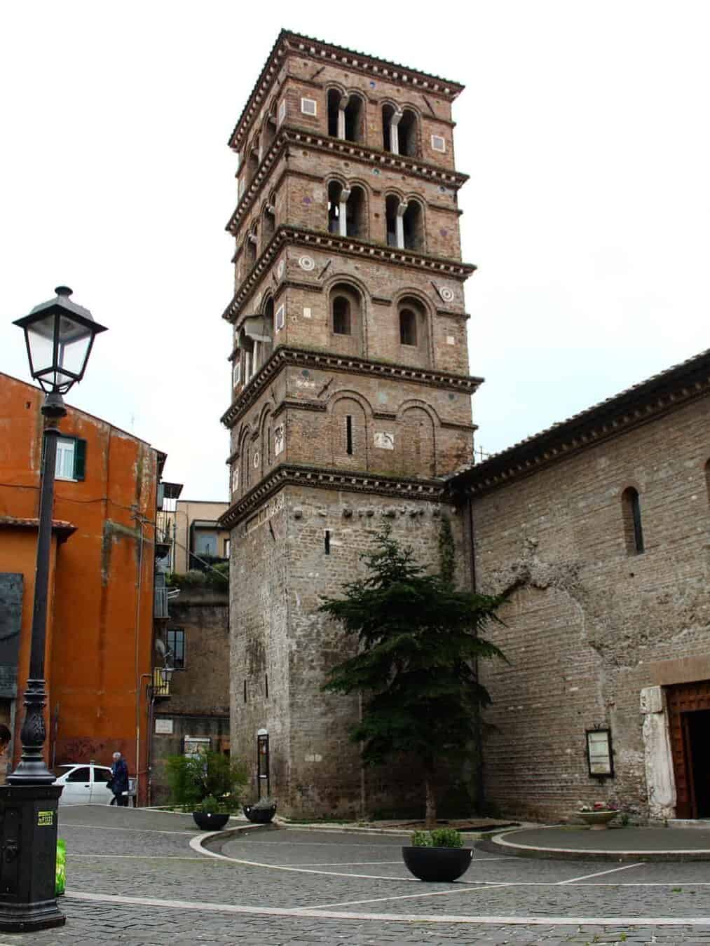 Tall, ancient brick bell tower with arched windows stands in a cobblestone square beside older buildings—a must-see during 4 days in Castel Gandolfo.