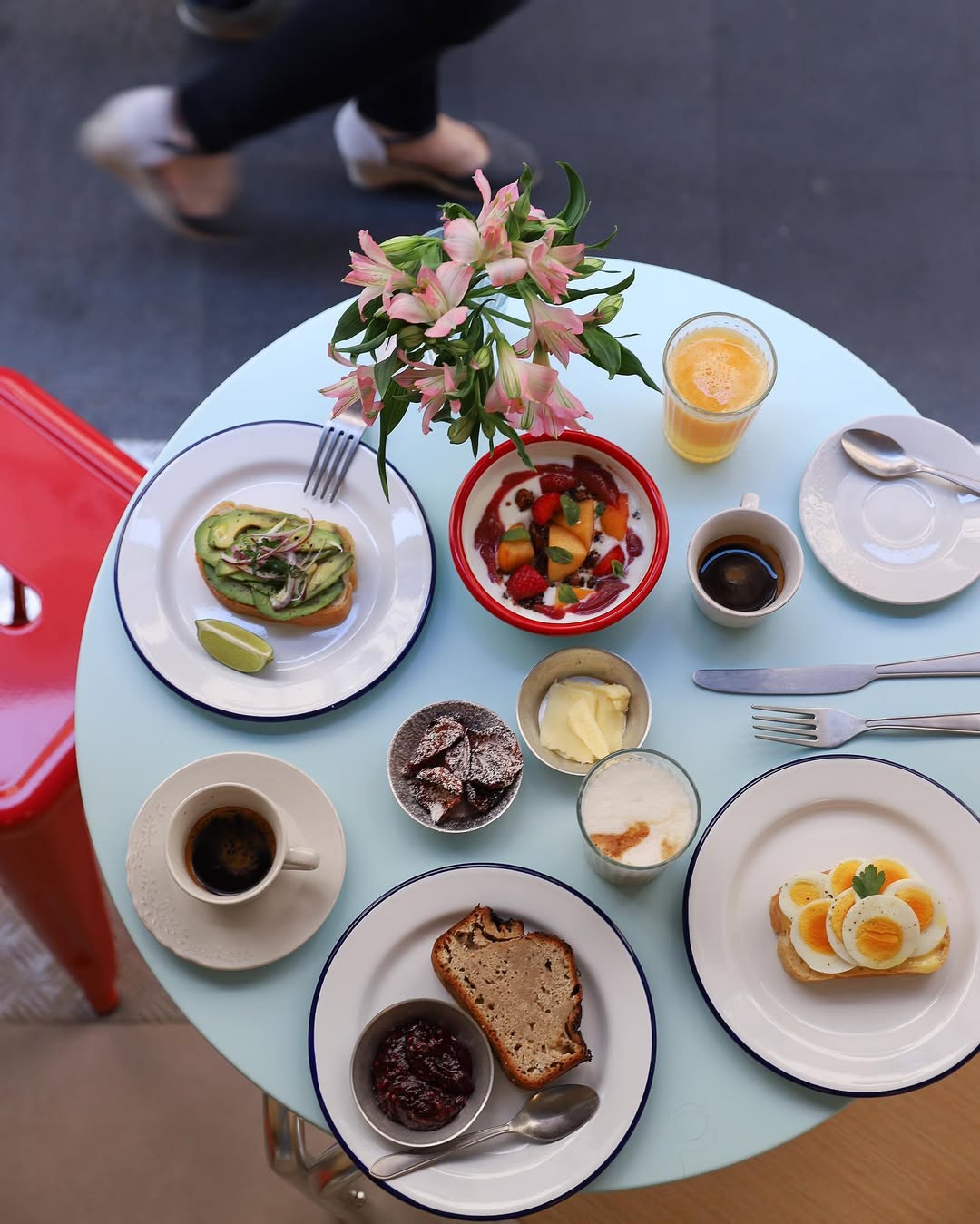 Round table with breakfast foods from Gluten Free Restaurants in Rome, coffee, juice, flowers, and a person walking by in the background.