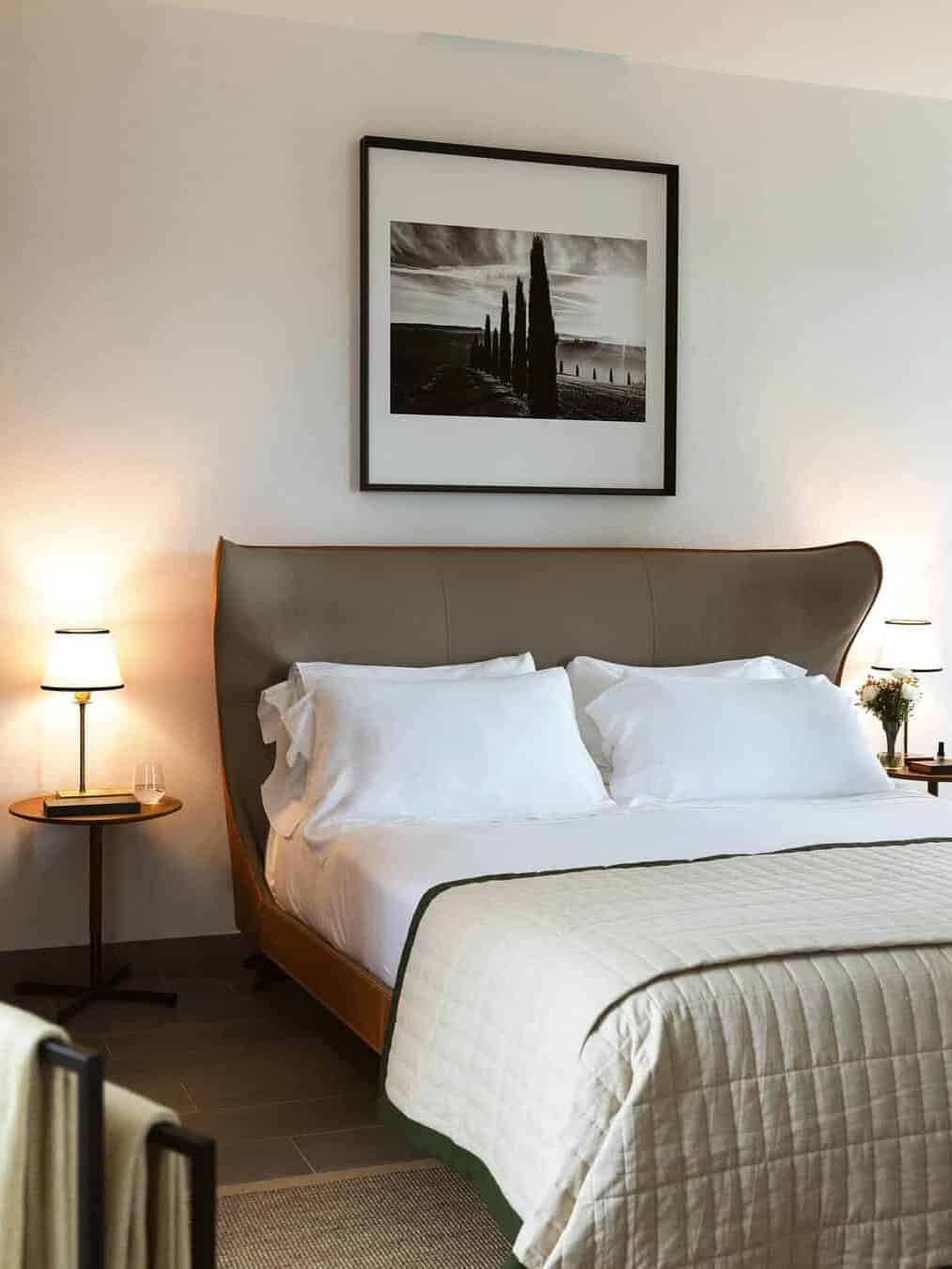 A neatly made bed with white linens, bedside tables with lamps, and a black-and-white photo above the headboard evoke the serene style found at the best beach resorts in Italy for families.
