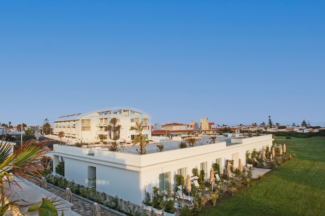 Modern white buildings with greenery in front, under a clear blue sky, next to an open green lawn&mdash;evoking the relaxed atmosphere found at the best beach resorts in Italy for families.