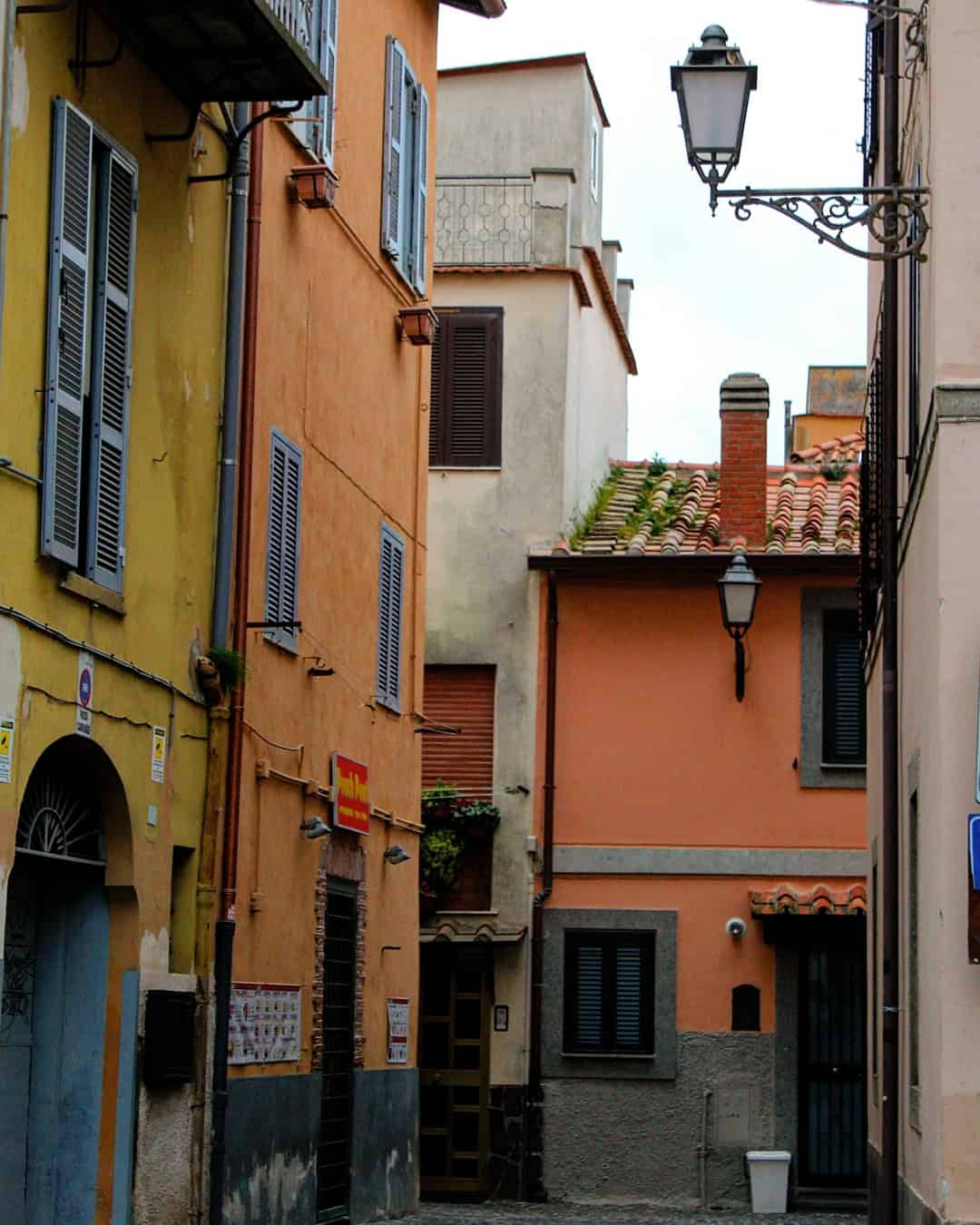 Narrow European street lined with colorful buildings, shuttered windows, and a vintage street lamp—perfect for capturing memories during 4 days in Castel Gandolfo.