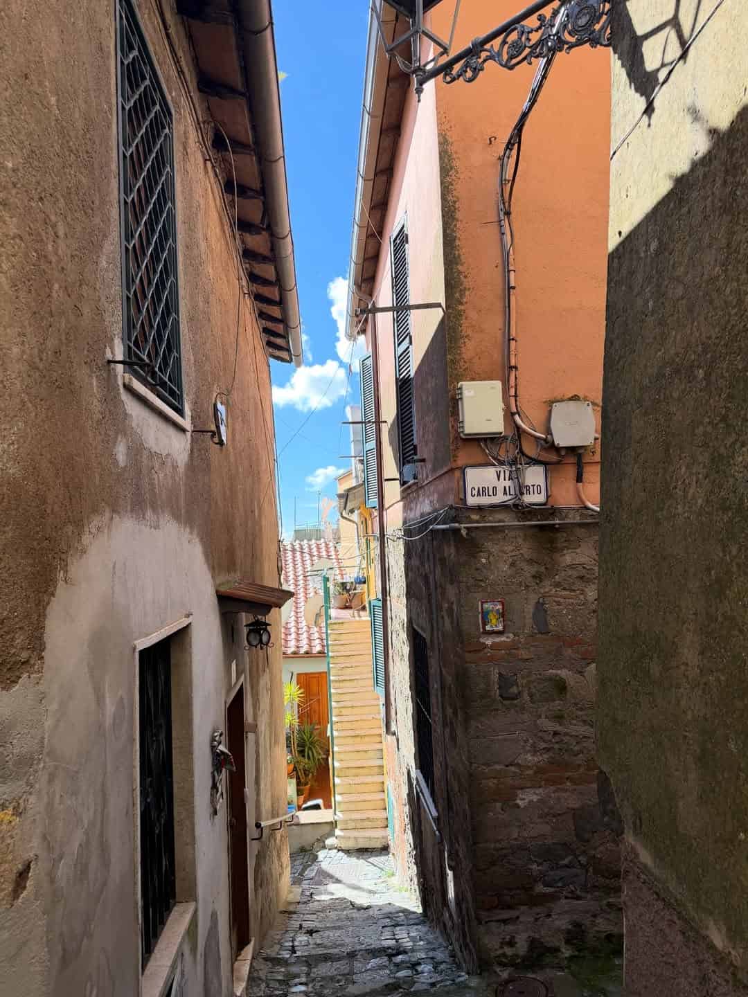 Narrow cobblestone alley with colorful buildings and stairs leading up under a bright blue sky, perfect for exploring during 4 days in Castel Gandolfo.
