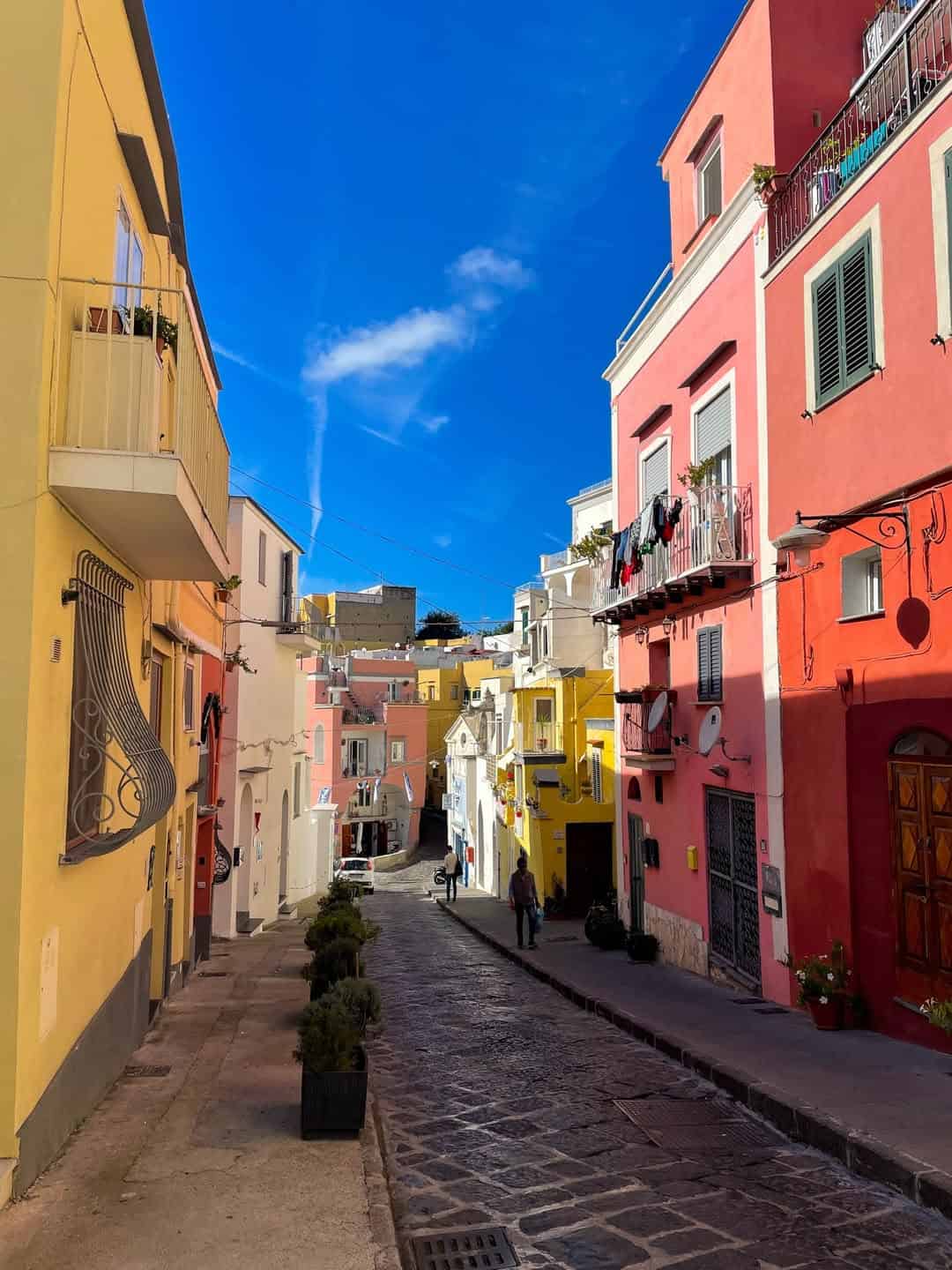 Colorful buildings line a narrow cobblestone street under a bright blue sky in a Mediterranean town, one of the best day trips from Rome for families.