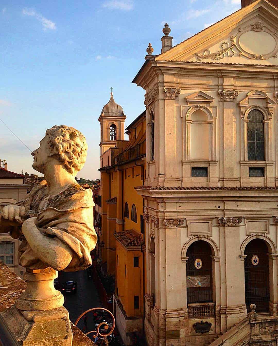 Stone statue overlooking an old European church and narrow street at sunset, with warm golden light&mdash;a scene reminiscent of the best day trips from Rome for families.