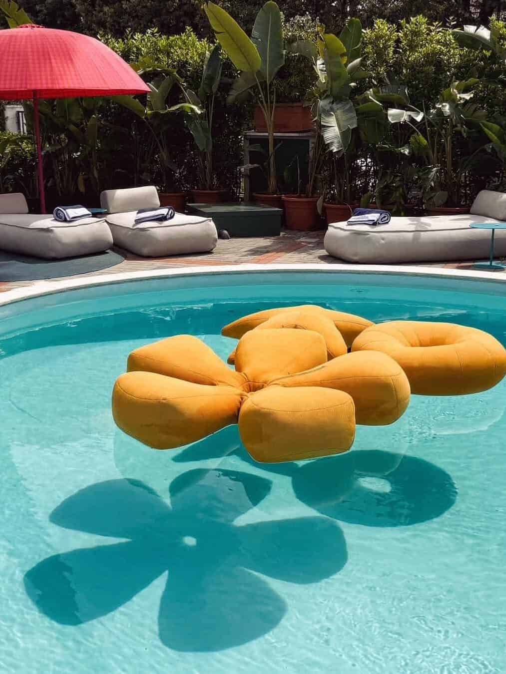 A yellow flower-shaped pool float in a clear blue pool&mdash;like those found at the best beach resorts in Italy for families&mdash;with lounge chairs and lush plants in the background.
