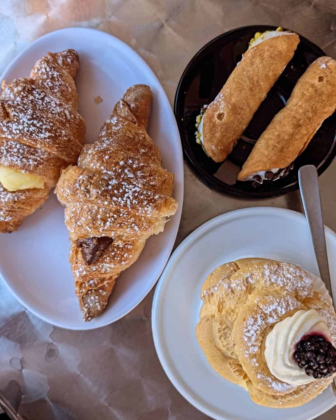 Three croissants, two cannoli, and a cream-filled pastry on plates, all dusted with powdered sugar—perfect for anyone exploring Gluten Free Restaurants in Rome looking for delicious treats.