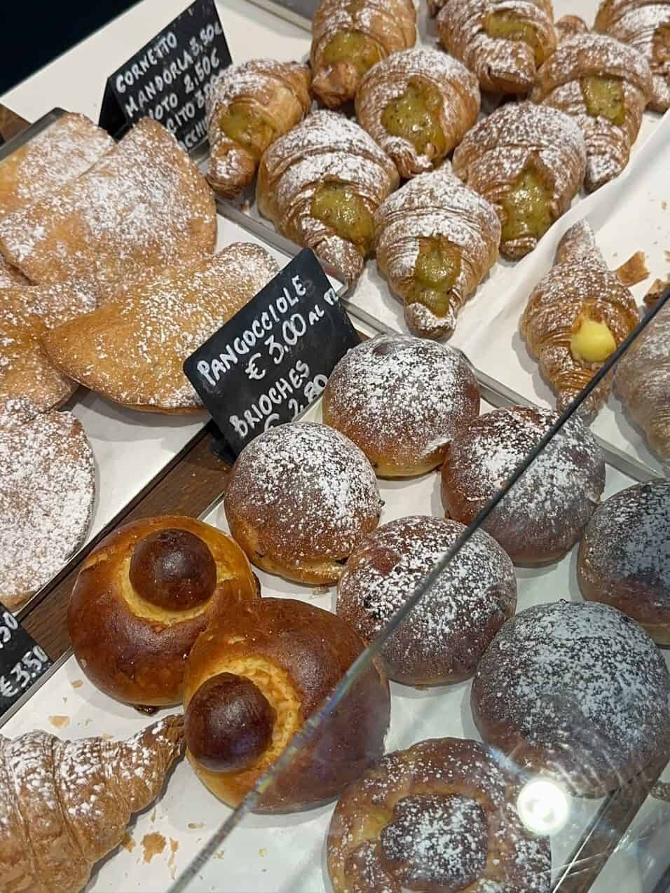 Assorted Italian pastries, including croissants and brioche, displayed behind glass with powdered sugar topping—perfect for those exploring gluten free restaurants in Rome.