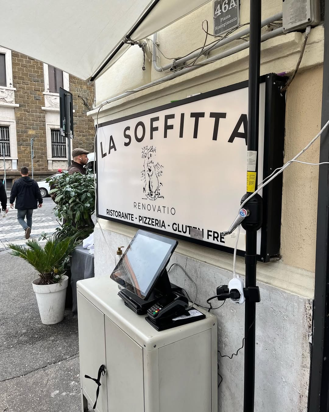 Outdoor sign for "La Soffitta" restaurant, known among Gluten Free Restaurants in Rome, with a computer and potted plants nearby on the sidewalk.