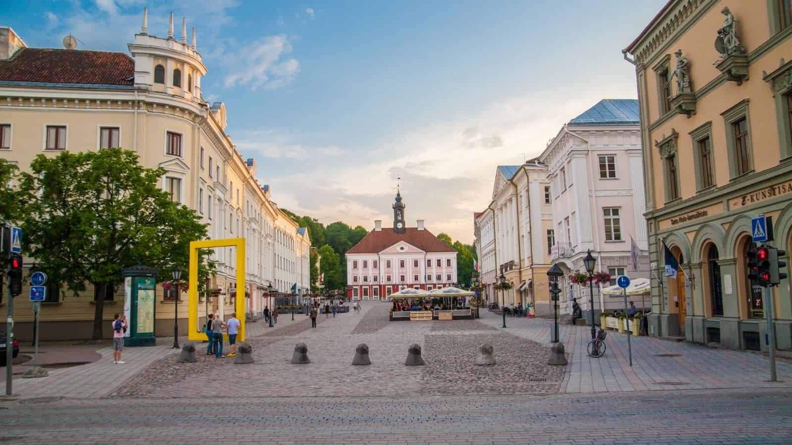 A cobblestone square with historic buildings and a central town hall under a blue sky at sunset.