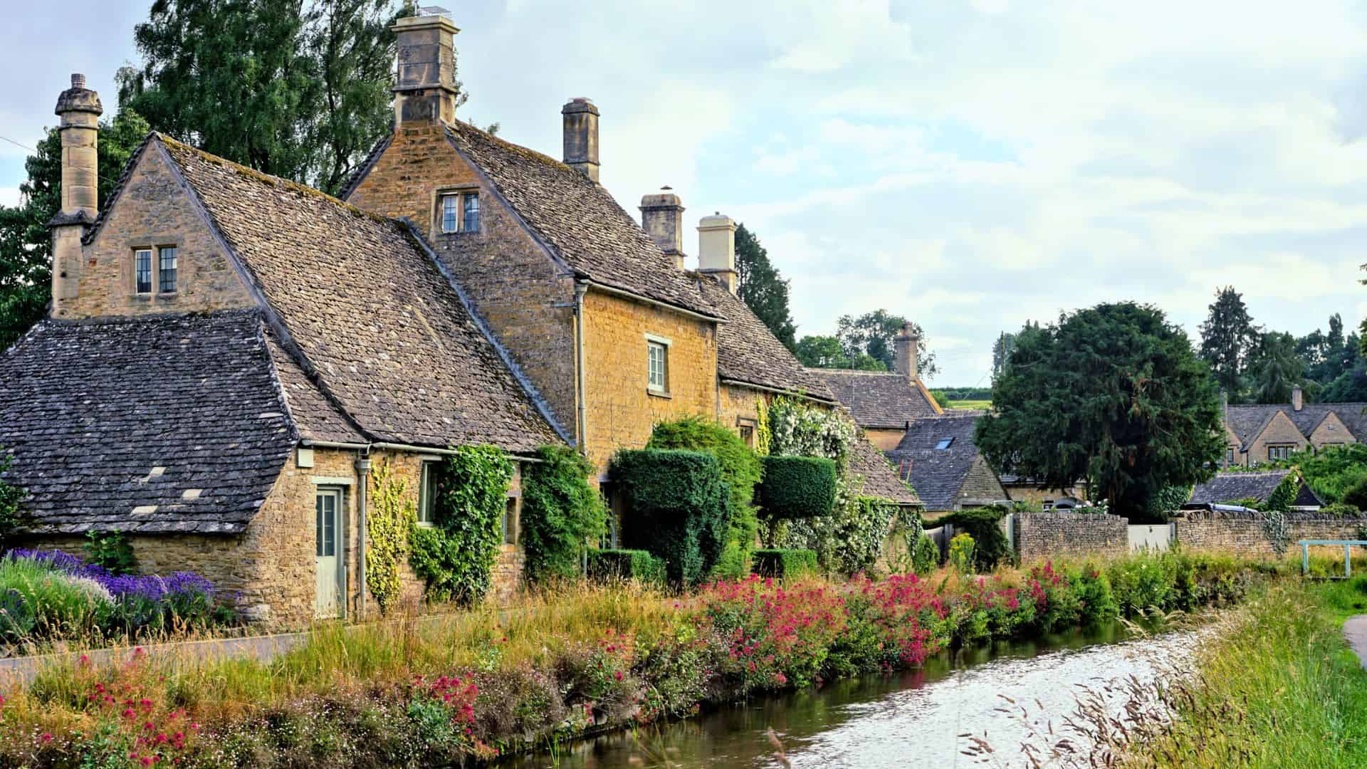 Stone cottages with ivy and flowers beside a narrow canal in a peaceful countryside village.