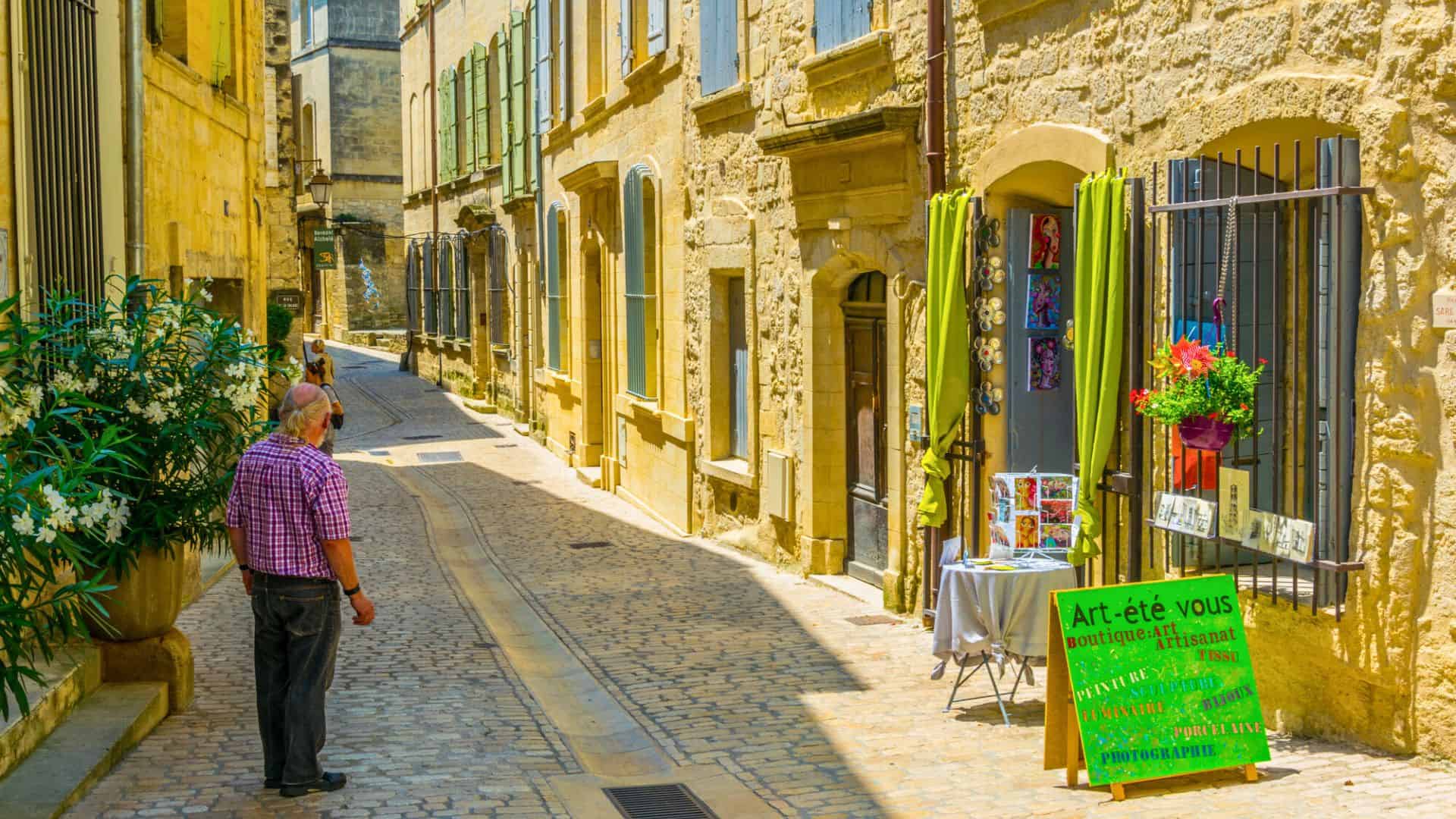 Sunny cobblestone street with art on display, a man observing, and a bright green sign in French.
