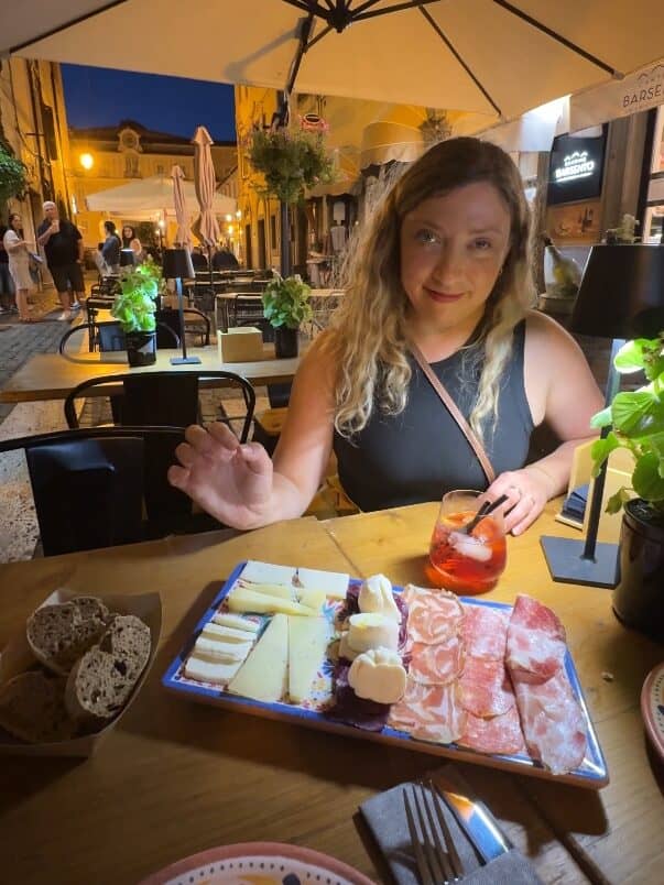 A woman enjoys cheese, meats, bread, and a drink at an outdoor restaurant table at night during her 4 days in Castel Gandolfo.