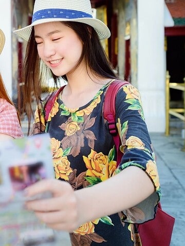Two young women in hats smiling and looking at a map outdoors, with a temple in the background.