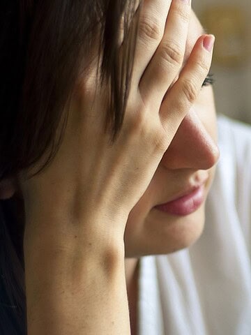 A woman sits with her hand covering her face, appearing stressed or overwhelmed.