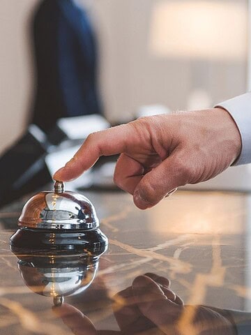 A person in a blue suit presses a service bell on a marble hotel reception desk.