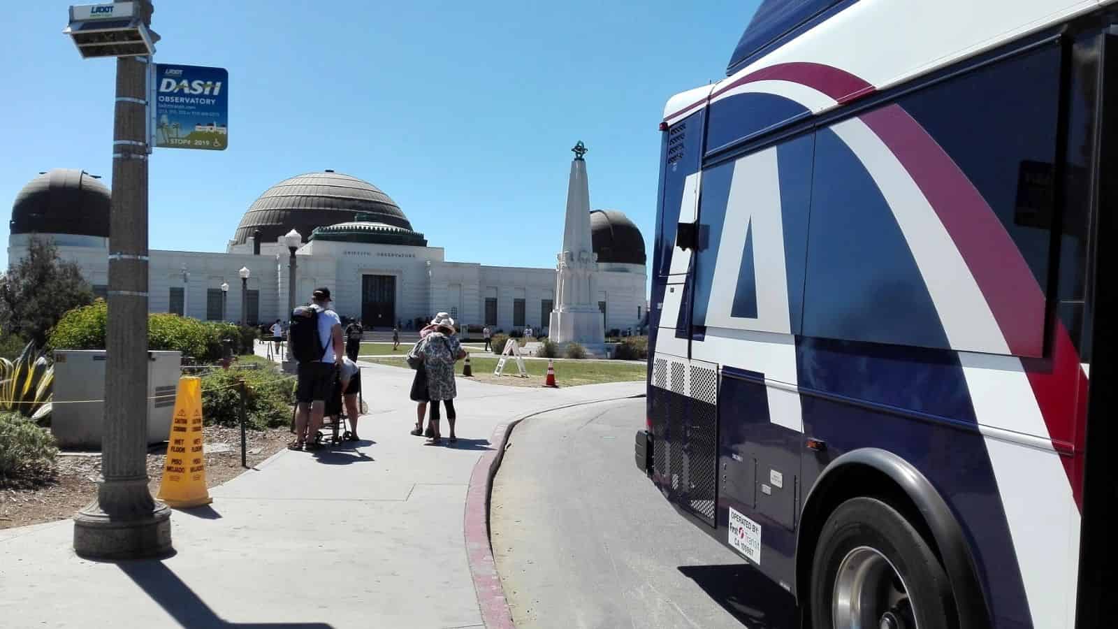 A bus parked near the Griffith Observatory on a sunny day with people walking toward the entrance.