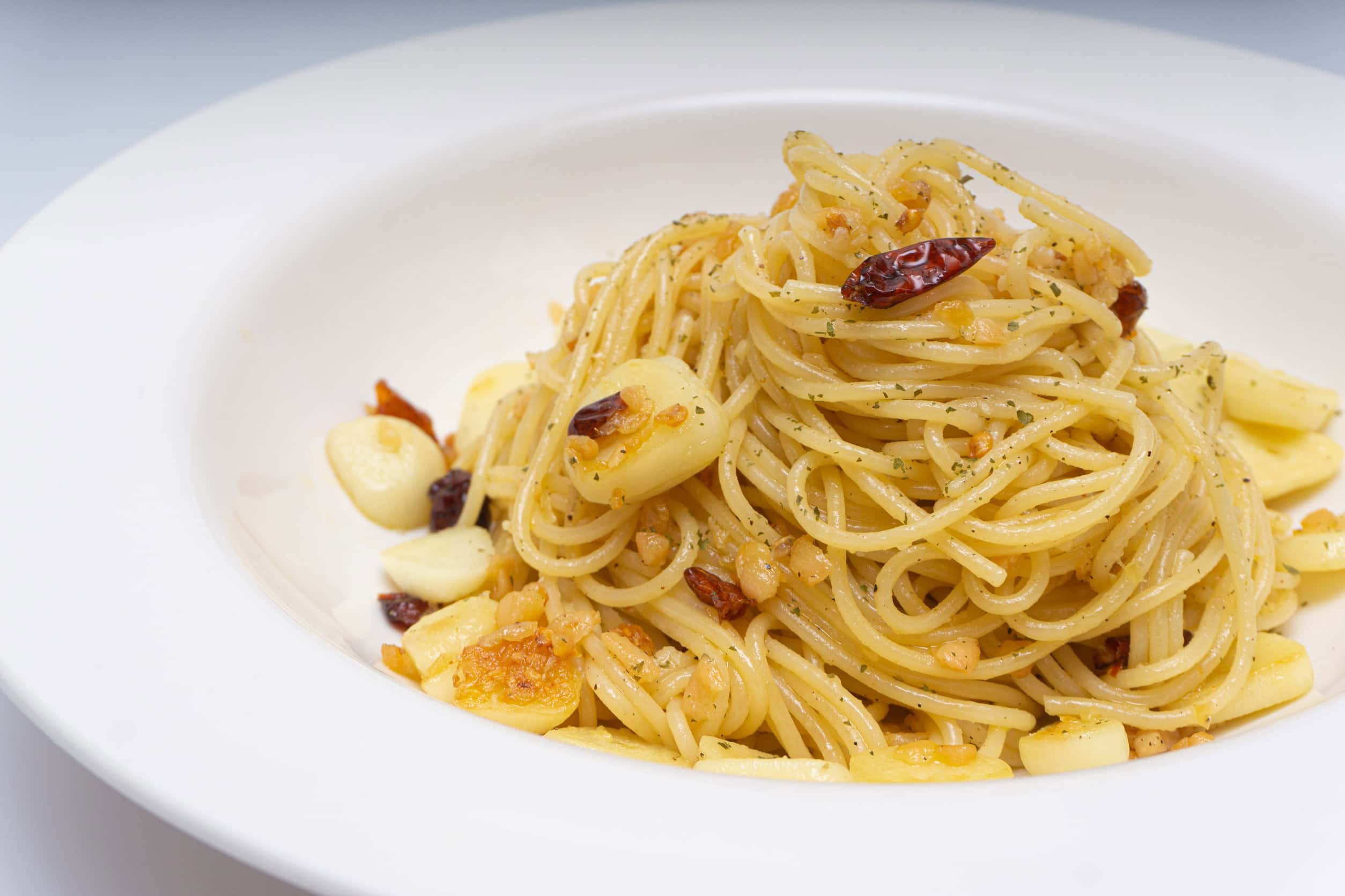 A white plate of spaghetti aglio e olio with garlic slices and red chili flakes&mdash;a delicious way to Eat Vegetarian in Italy.