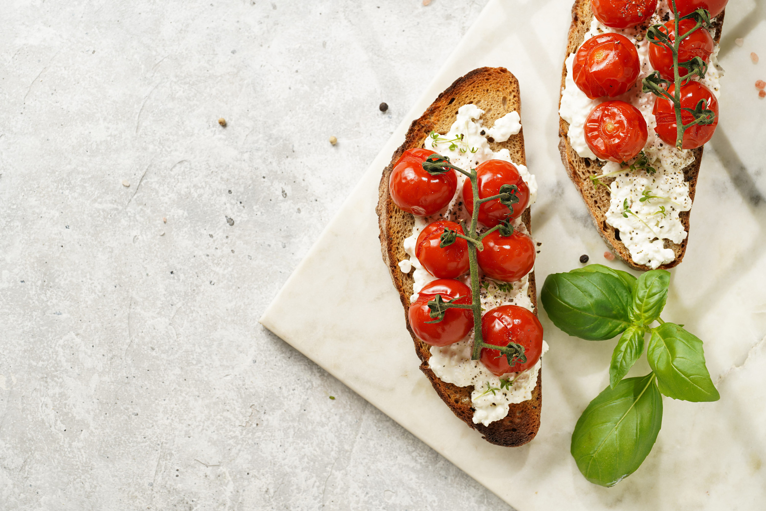 Two slices of toast with ricotta cheese, roasted cherry tomatoes, and basil on a marble board&mdash;a perfect way to Eat Vegetarian in Italy.