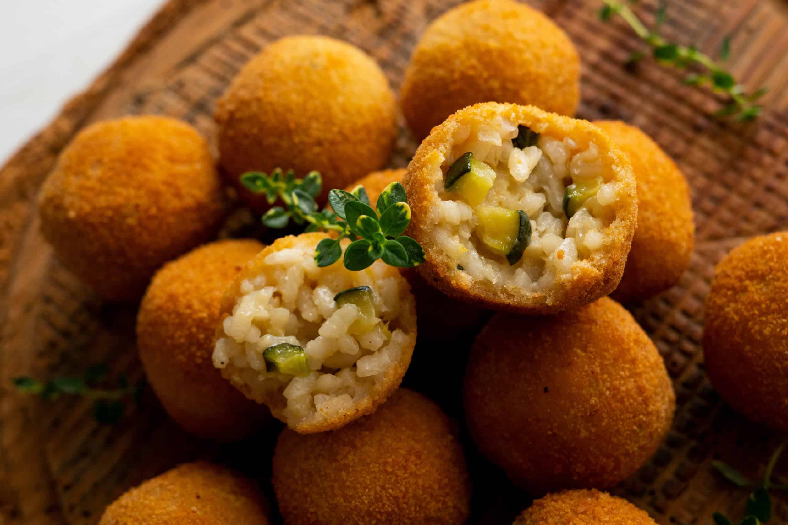 Golden arancini balls, one cut open to show rice and vegetable filling, garnished with fresh herbs&mdash;a delicious way to eat vegetarian in Italy.