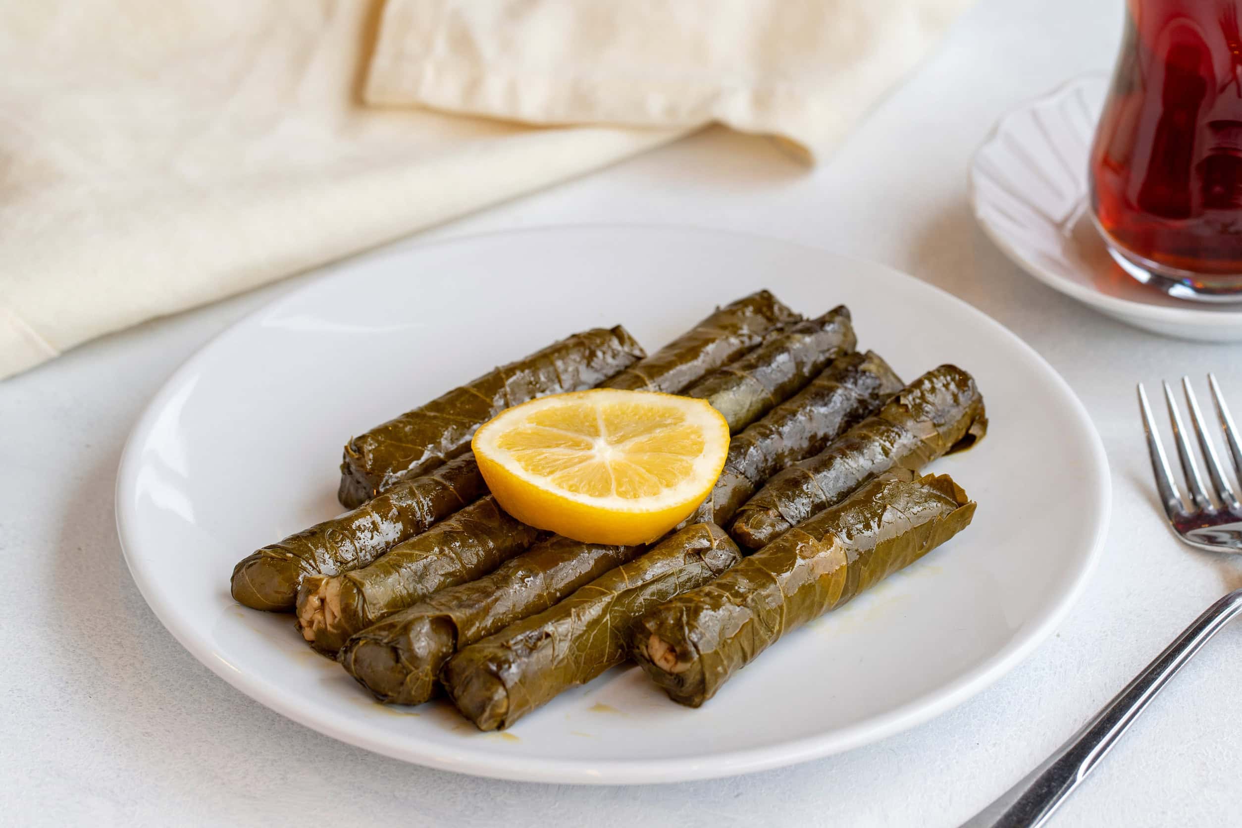 Stuffed grape leaves arranged on a white plate, garnished with a lemon slice, with a fork and tea nearby&mdash;an inviting example of authentic Vegetarian Food in Israel.