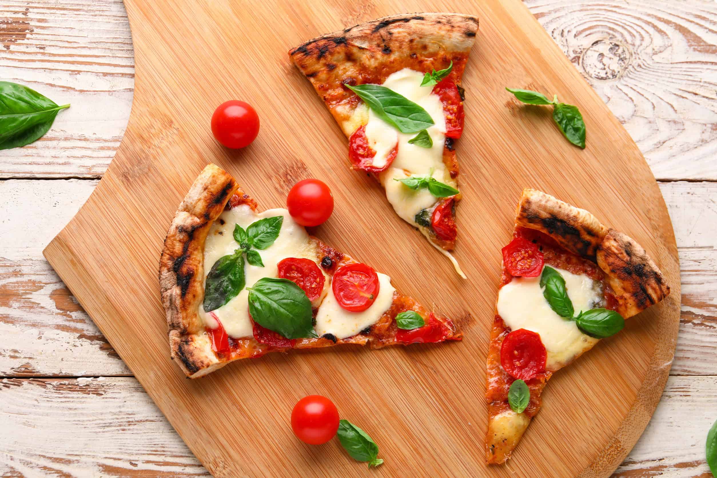 Three slices of pizza with tomatoes, mozzarella, and basil on a wooden board&mdash;perfect for those looking to eat vegetarian in Italy. Cherry tomatoes are scattered nearby, adding fresh flavor to this classic dish.