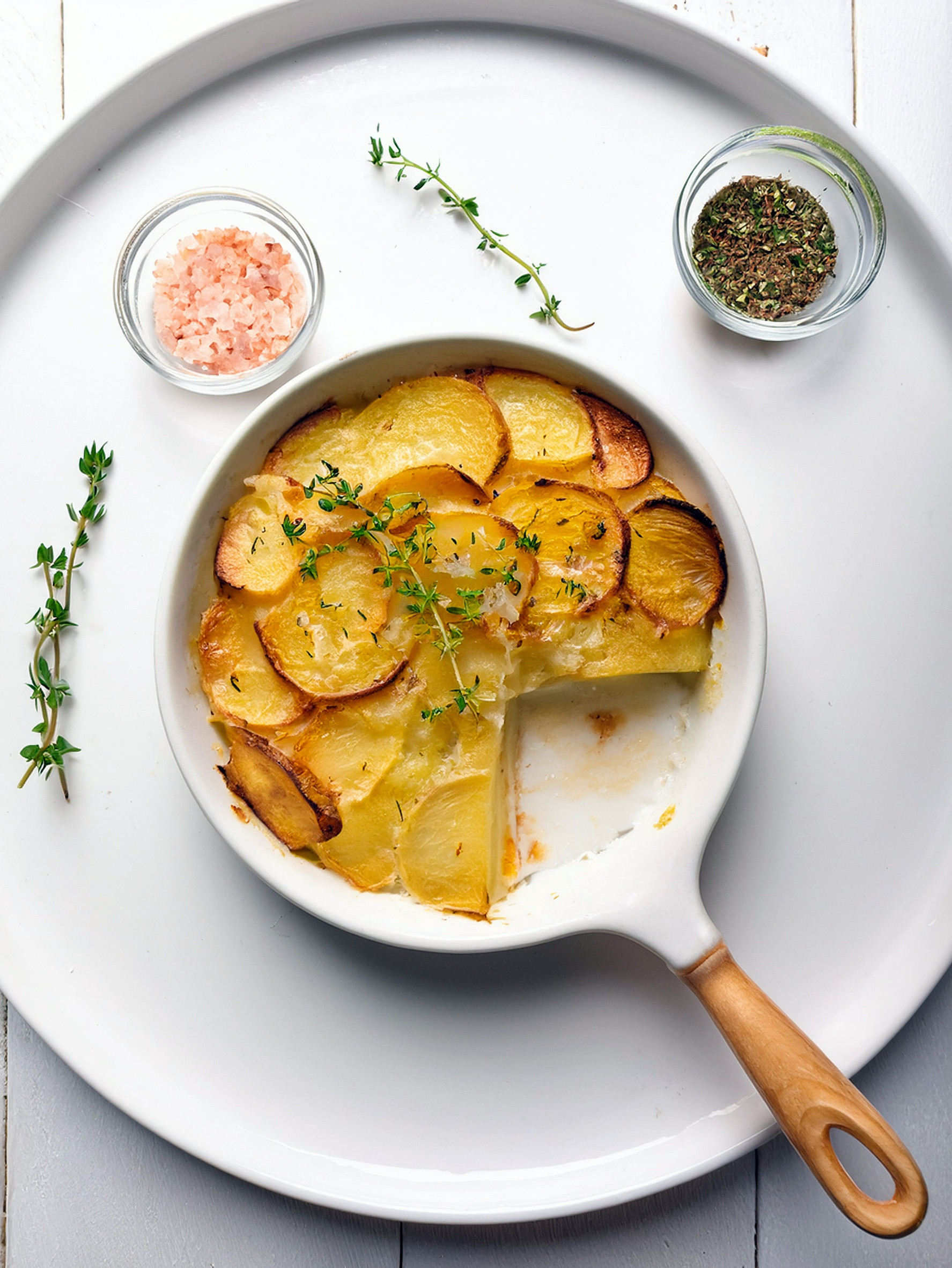 A baked potato dish in a white pan with herbs, pink salt, and dried spices on a white tray&mdash;an example of the Best Vegetarian Food in France.