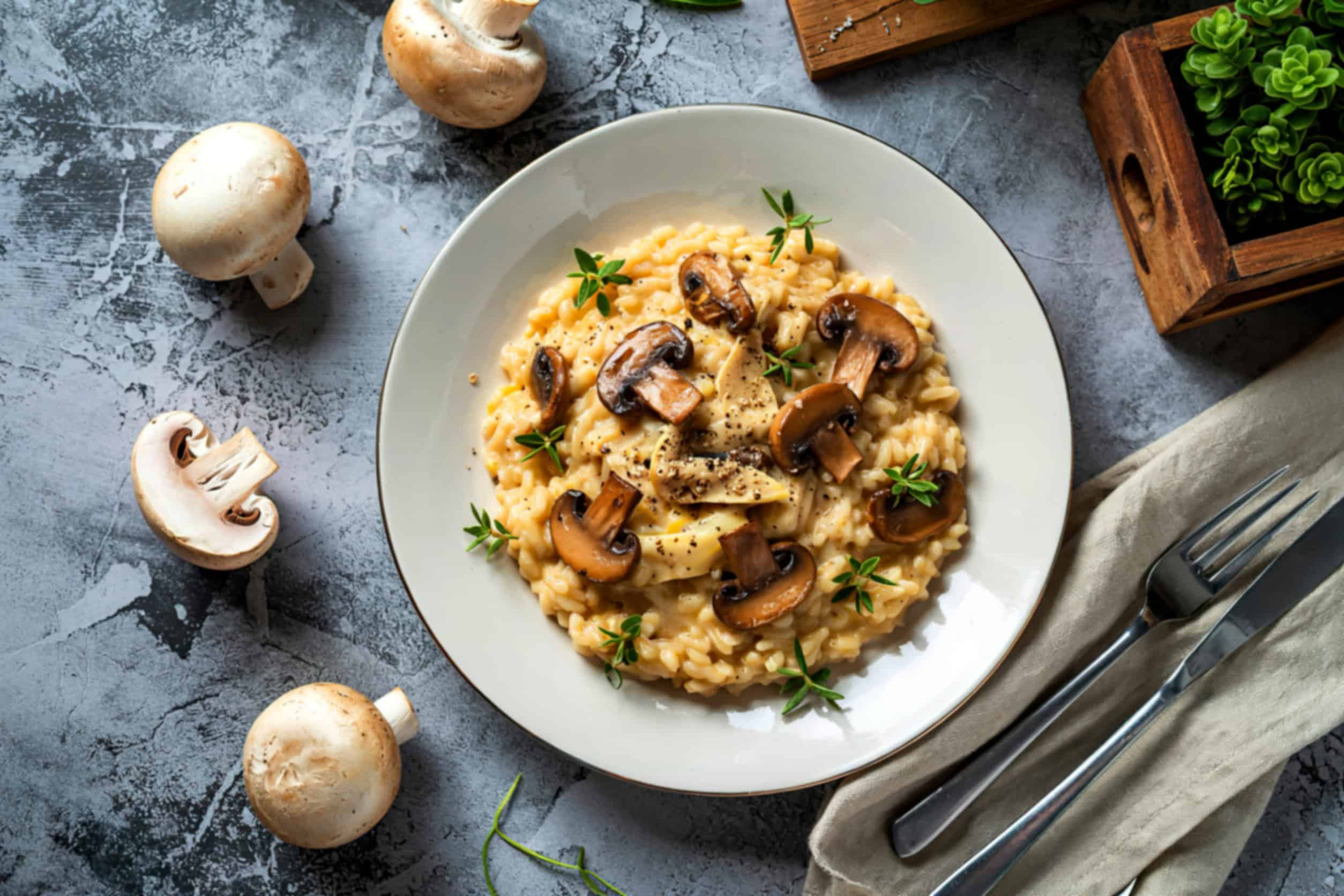 A plate of creamy mushroom risotto garnished with fresh herbs, perfect for those looking to eat vegetarian in Italy, with mushrooms and cutlery on the side.