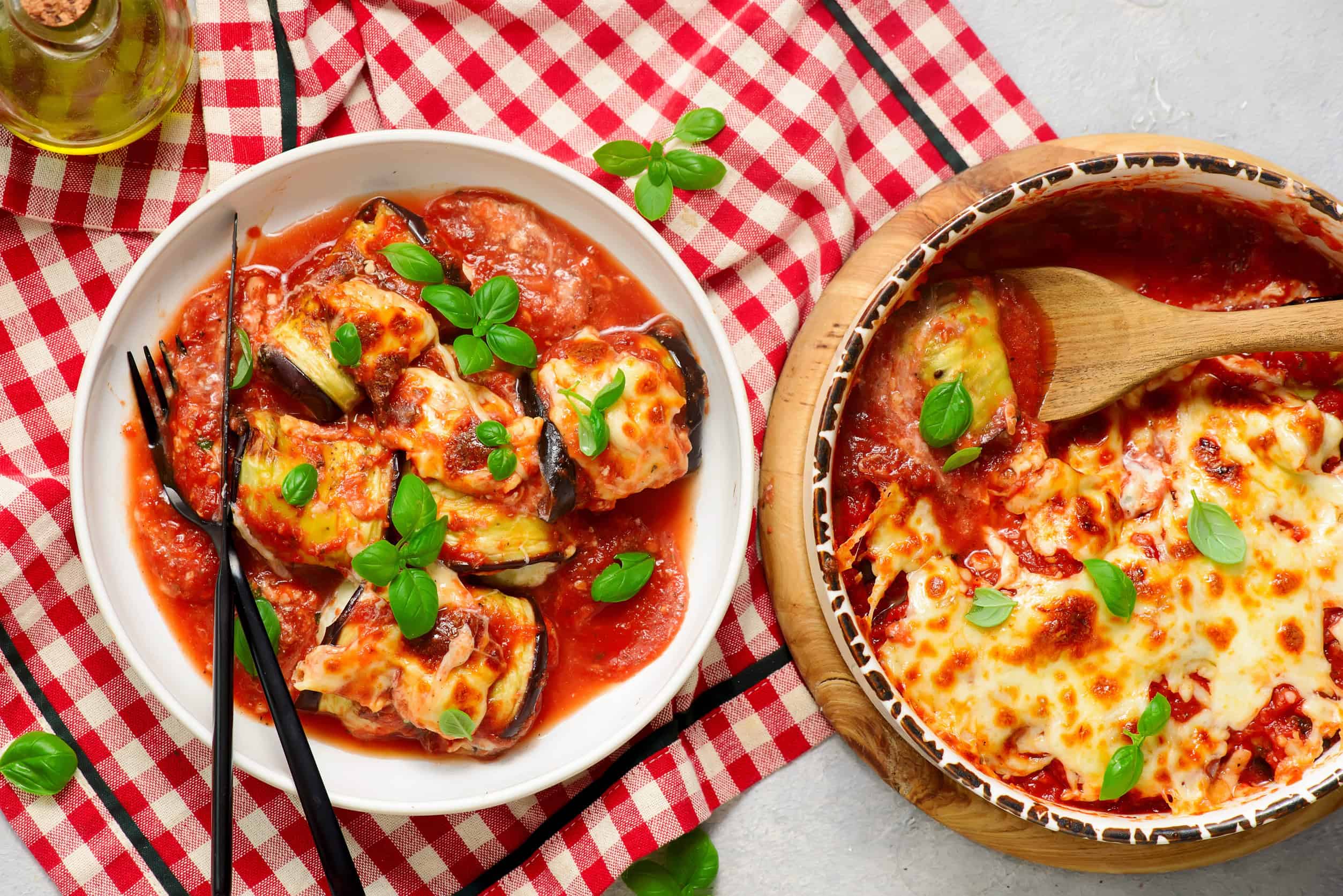 Baked eggplant rollatini with tomato sauce and melted cheese, garnished with basil on a red checkered cloth&mdash;a perfect way to eat vegetarian in Italy.