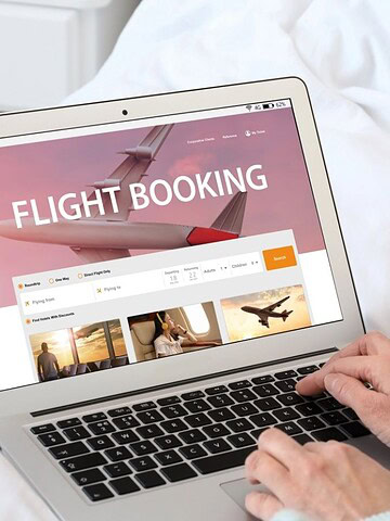 Person using a laptop to book a flight online while sitting on a bed.