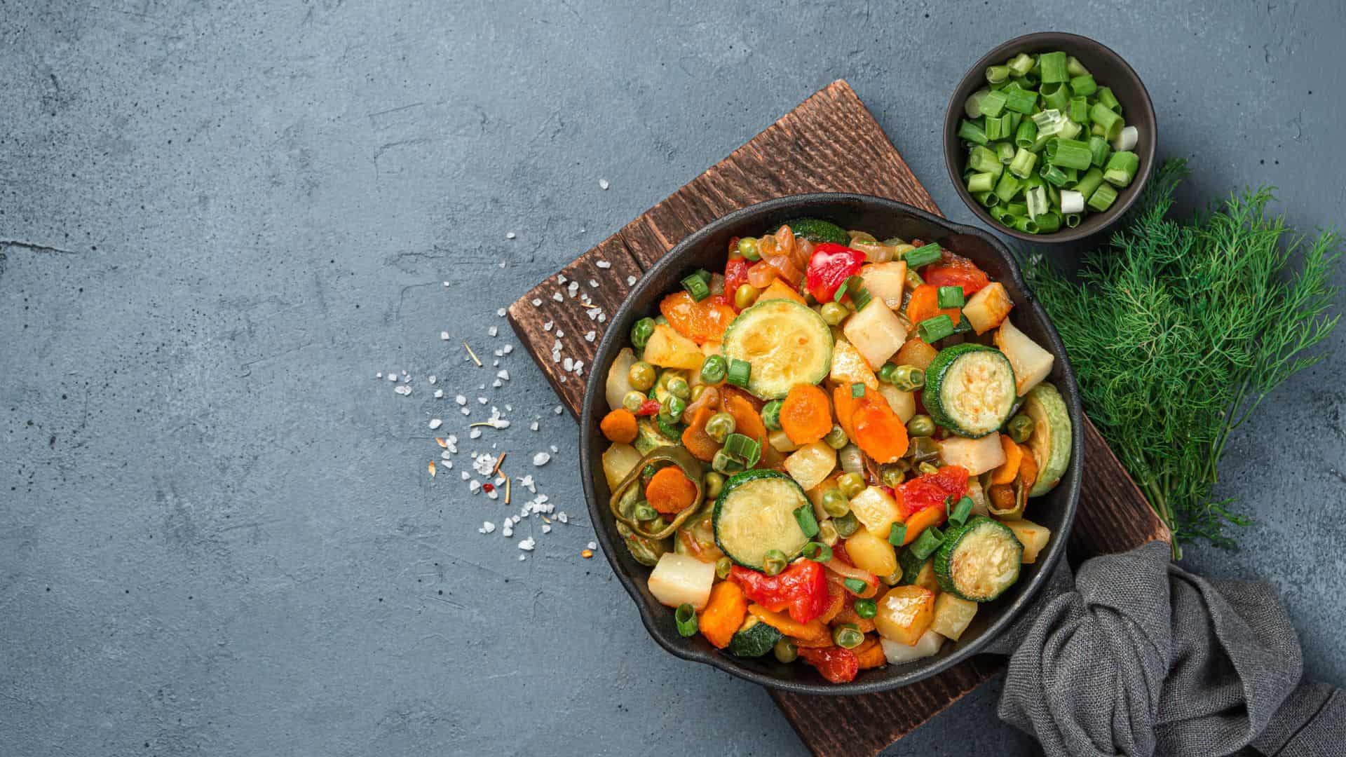 A skillet of colorful saut&eacute;ed vegetables, inspired by the Best Vegetarian Mexican Dishes, sits beside a bowl of chopped green onions on a wooden board.