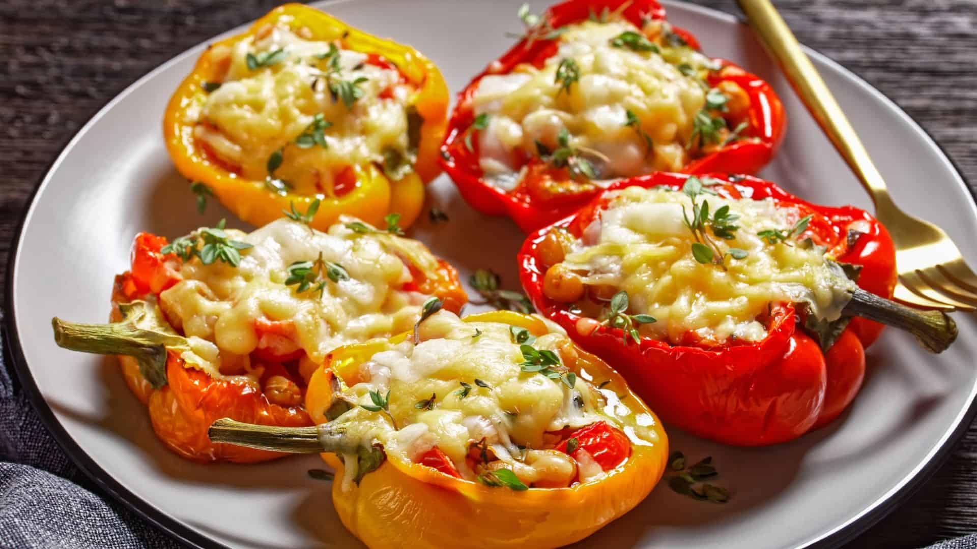 Stuffed red and yellow bell peppers topped with melted cheese and herbs, served on a plate with a gold fork&mdash;one of the Best Vegetarian Mexican Dishes to savor.