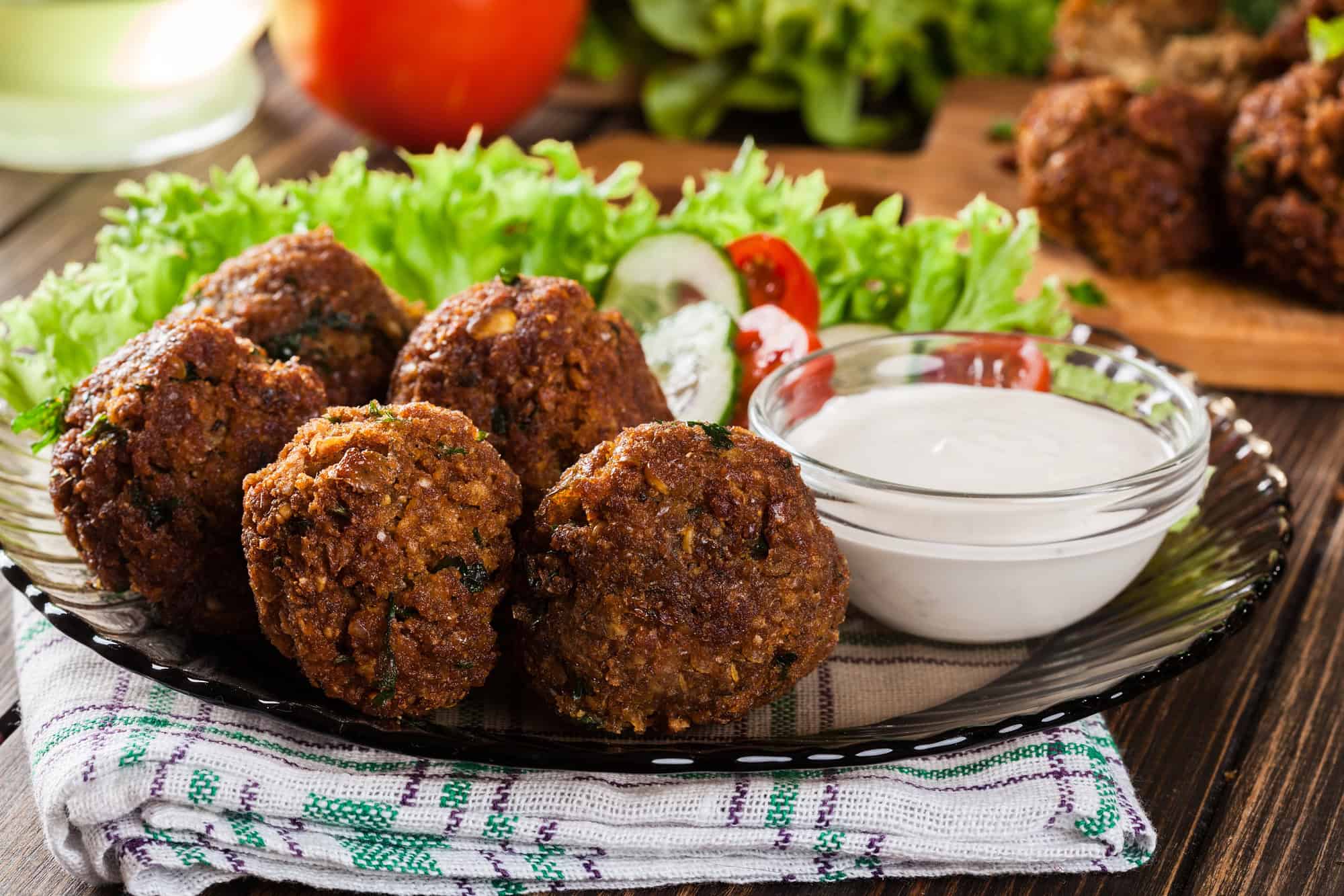 Four falafel balls on a plate with lettuce, sliced vegetables, and a bowl of white dipping sauce&mdash;a classic example of delicious vegetarian food in Israel.