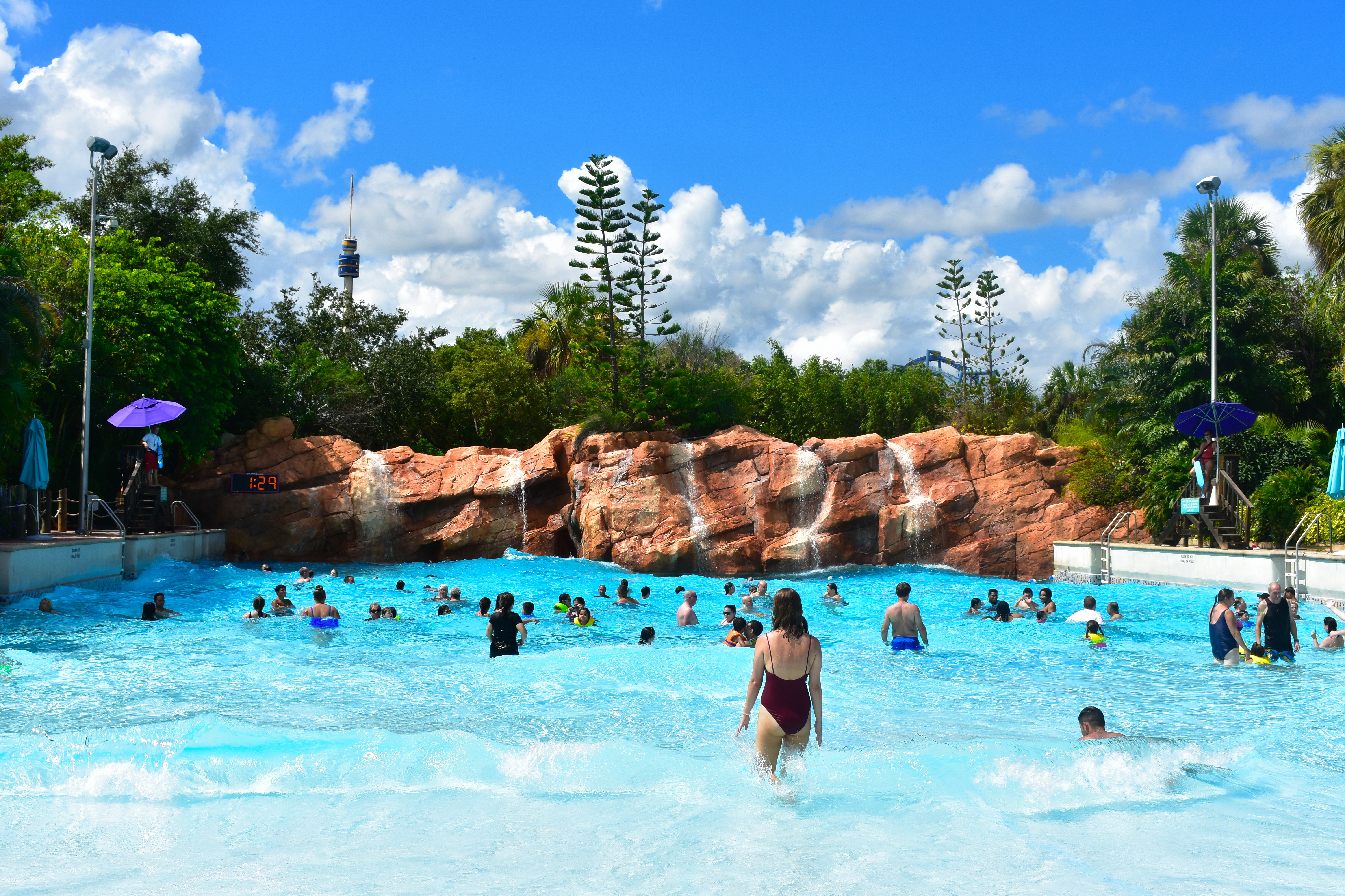 Families enjoying a wave pool at a bucket list water park, surrounded by rocks and lush greenery under a blue sky&mdash;a perfect family travel destination.
