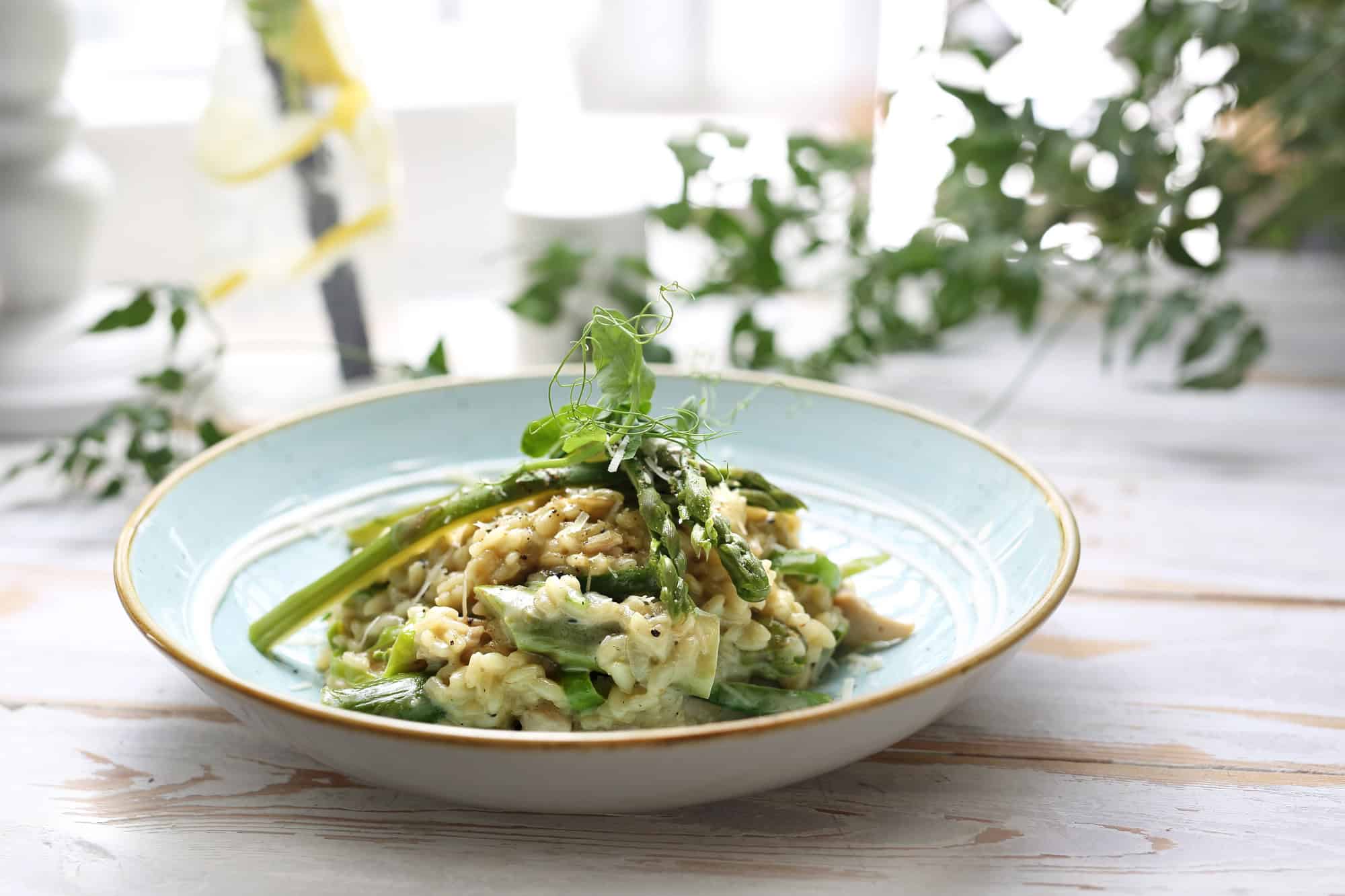 A plate of creamy risotto topped with asparagus and fresh herbs on a light wooden table, this dish is a delicious take on Canadian Vegetarian Dishes.