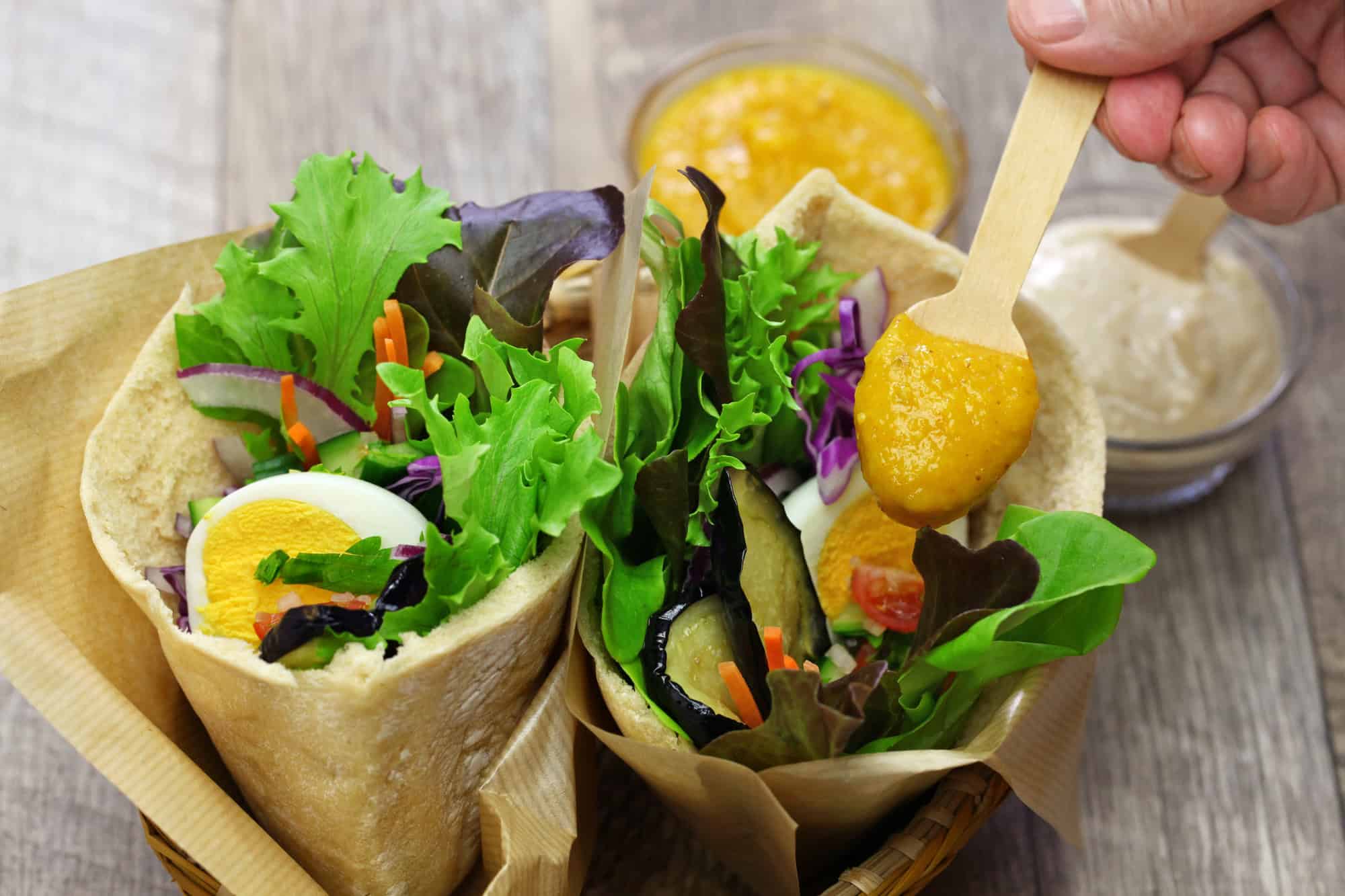 Two pita wraps filled with leafy greens, egg, and vegetables&mdash;a classic example of vegetarian food in Israel&mdash;served with a flavorful sauce spooned on top.