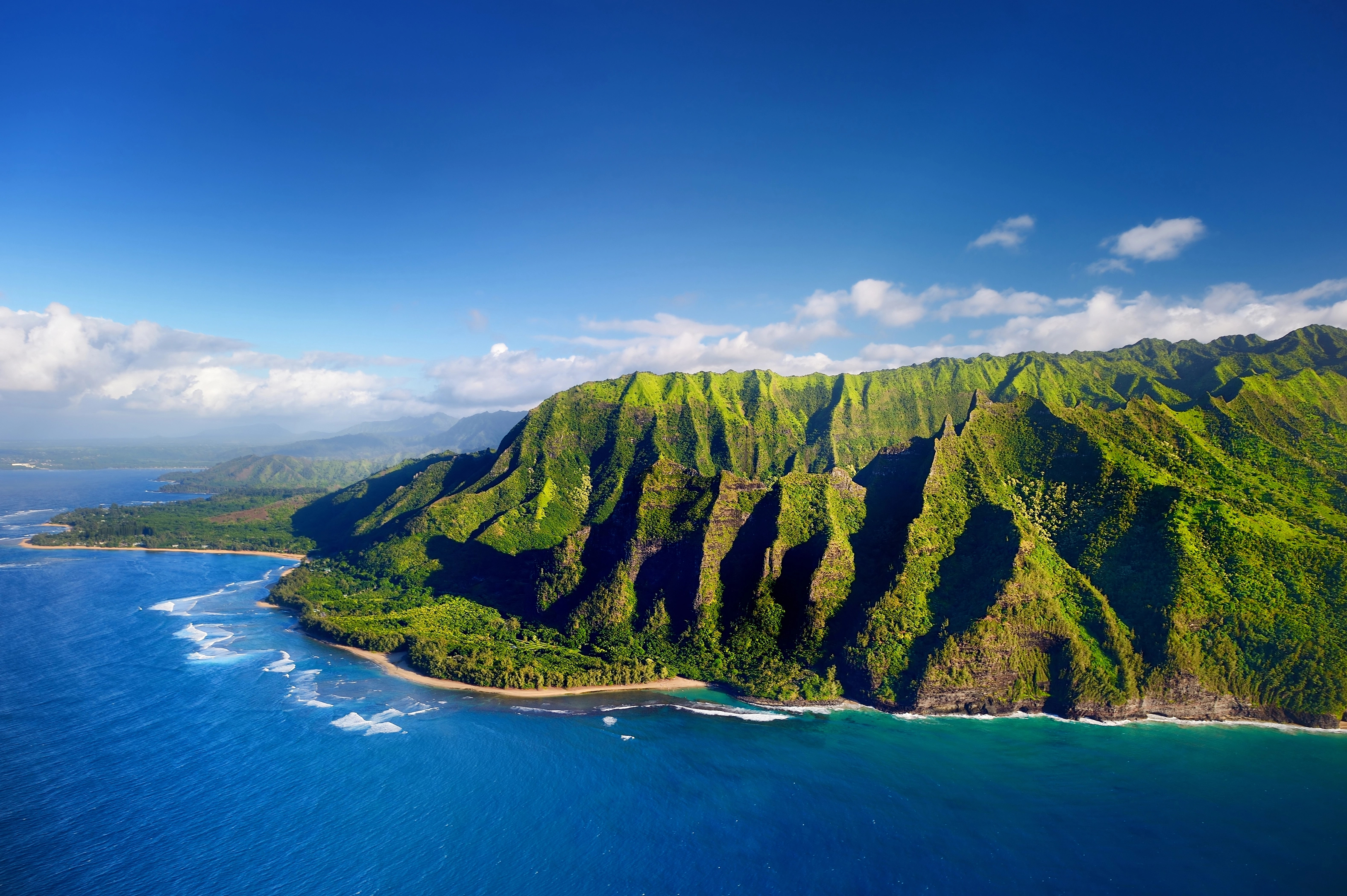 Aerial view of a lush, green, mountainous coastline with blue ocean waves and a sunny sky&mdash;perfect for your bucket list of unforgettable travel destinations.