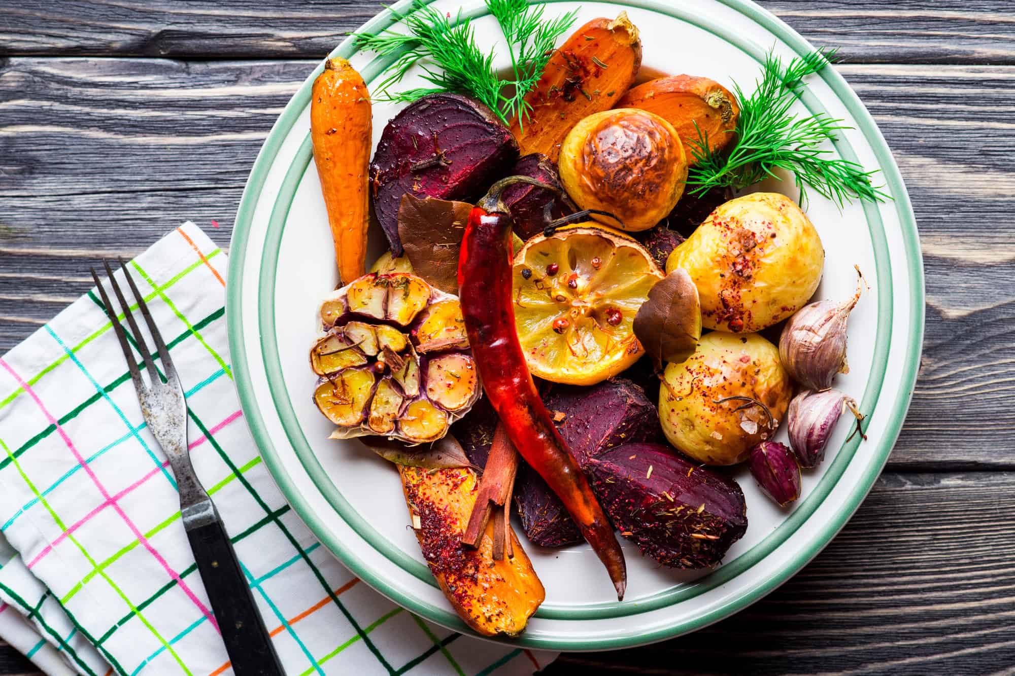 Plate of roasted vegetables&mdash;including potatoes, carrots, beets, garlic, and herbs&mdash;showcases the vibrant flavors found in Canadian Vegetarian Dishes on a rustic wooden table.
