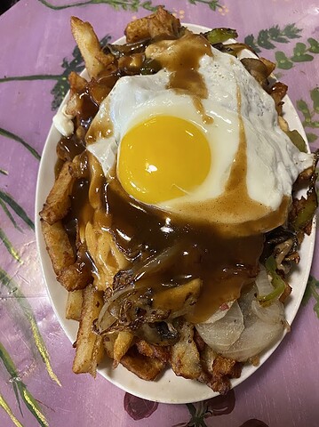 A plate of fries topped with onions, peppers, a fried egg, and brown gravy on a pink floral table—an inviting twist on Canadian vegetarian dishes.