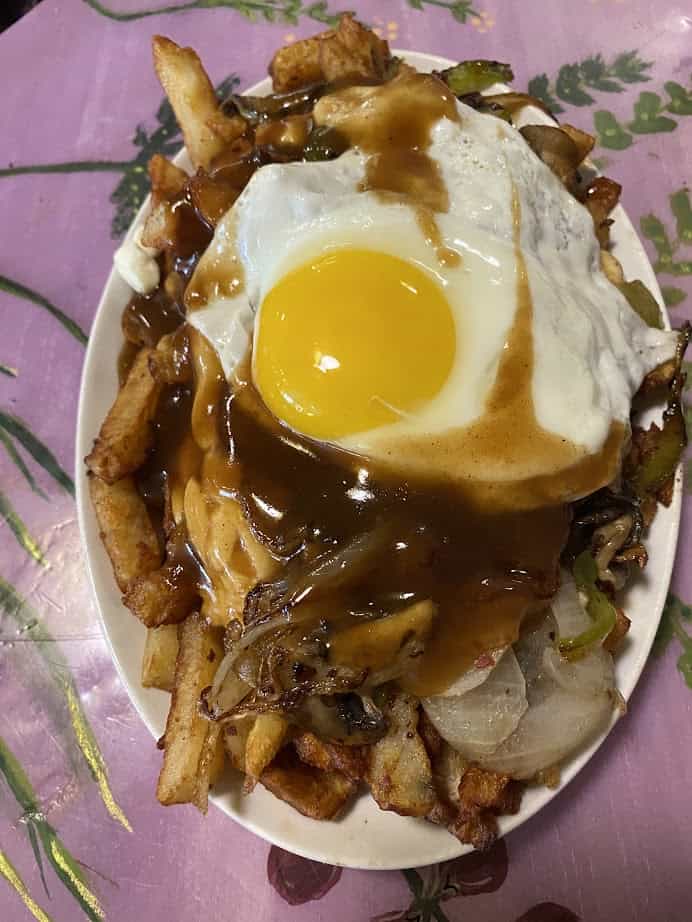 A plate of fries topped with onions, peppers, a fried egg, and brown gravy on a pink floral table&mdash;an inviting twist on Canadian vegetarian dishes.