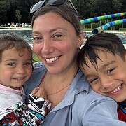 Smiling woman with two children at a pool, surrounded by waterslides and trees—a perfect family travel moment at one of the top bucket list travel destinations.