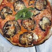 Experience authentic Italian flavor with this pizza topped with roasted eggplant, tomato sauce, cheese, and fresh basil—a delicious way to Eat Vegetarian in Italy.