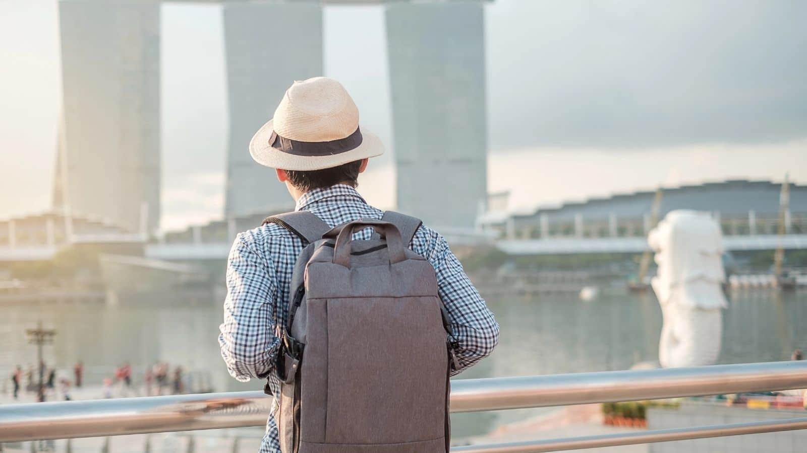 Person wearing a hat and backpack looks at Marina Bay Sands and the Merlion statue in Singapore.