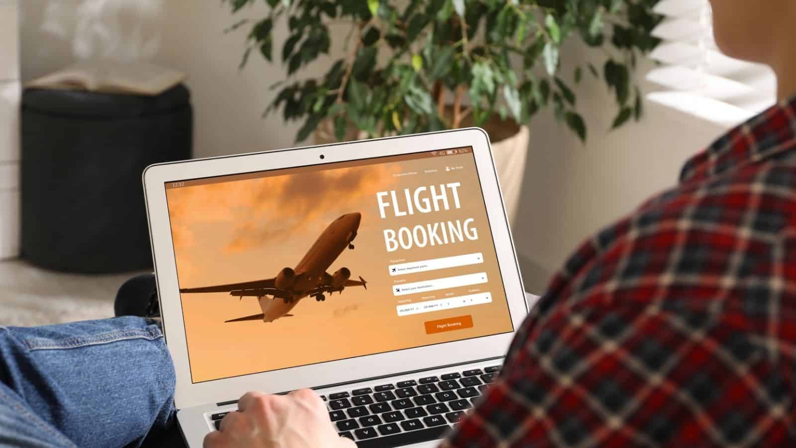 Person using a laptop to book a flight online, with an airplane image and booking form visible on the screen.