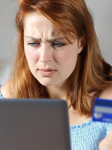 A concerned woman looks at her laptop while holding a credit card.