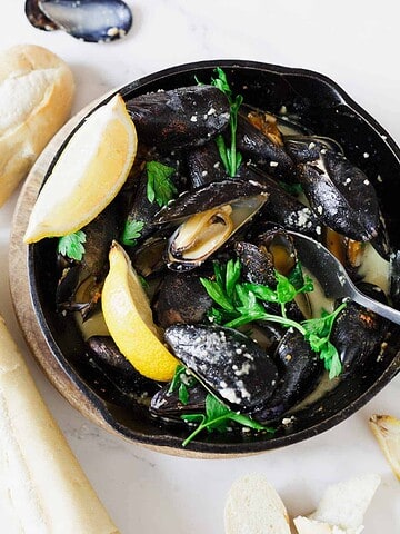 A bowl of steamed mussels in a creamy sauce with lemon wedges, fresh parsley, and baguette slices—a coastal classic often enjoyed alongside the best vegetarian food in France.